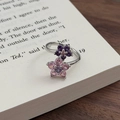 Makroaufnahme eines silbernen Blumenrings mit rosa und lila Zirkonia auf Buchseiten - Einstellbar Offen / Doppelblumen-Stil (JZ3879A)