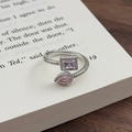 Detail eines verstellbaren Silberrings mit violetten und rosa Steinen auf einem Buch - Einstellbar Offen