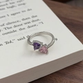 Detail eines Bypass-Rings mit lila und rosa Herzsteinen auf einer antiken Buchseite - Einstellbar Offen / Doppelherz-Stil (JZ5725)