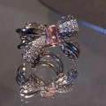 Elegant silver bow ring with a pink zircon center and pavé stones on a reflective surface - Left Ear