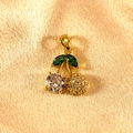 Close-up of a sparkling cherry pendant with green stones on yellow satin fabric - Gold Green Leaf White Inlaid Cherry Pendant