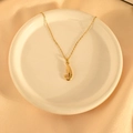 Gedetailleerd zicht op een vergulde J-hanger ketting op een elegante zijden achtergrond - Garnaalaas Stijl / Goud