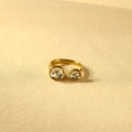 Detail van vergulde open ring met twee ronde sprankelende kristallen op satijnen stof - Witte Steen + Witte Steen