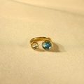 Detail van een gouden open ring met kristal en een diepblauwe ronde steen op satijn - Lichtblauwe Steen + Witte Steen
