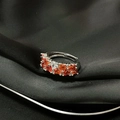 Detalle de anillo plateado con piedras naranjas sobre tela de seda negra mate - Estilo Diamantes Pave Naranja y Blanco (JZ4624)