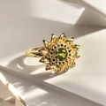 Primer plano de anillo de girasol dorado con piedra verde en fondo de bloques puros - Estilo Girasol con Gema Verde (JZ5563)