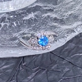 Vue macro d'une bague ouverte en argent avec gemme bleue et détails de nœud étincelants - Style Aérodynamique Asymétrique (JZ6269)
