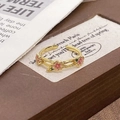 Details von rosa Emaille-Blumen und gewebtem Goldring auf Vintage-Zeitungs-Hintergrund - Einstellbar Offen / Rosa Emaille Drei Blumen Stil (JZ4323)