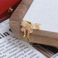 Vue macro d'une bague vintage dorée avec nœud en émail rose sur plateau en bois - Style Nœud Émail Rose Pâle (JZ6062)