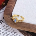 Gros plan détaillé d'une bague vintage dorée ornée d'une gemme bleue marquise et de zircons - Style Pétale Radial Pierre Marquise Bleue (JZ6094)