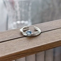 Detailed close-up of light blue oval zircon ring with wavy silver band on wooden surface - Wave Oval Blue Style (JZ5867)