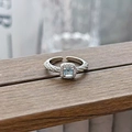 Close-up of aquamarine blue gemstone ring with halo diamonds on a rustic wooden surface - Square Blue Twist Style (JZ5679)