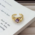 Makro-Detail des Vintage-Goldrings mit lila Zirkon auf antiken Buchseiten - Einstellbar Offen / Vintage Sternenhimmel Quadratischer Edelsteinstil (JZ5766) / Gold-Lila