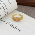 Détail macro d'une bague vintage en or avec zircon rose posée sur un livre classique - Design Aile Cœur Rose Doux (JZ0783A)