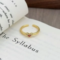Dettaglio di anello dorato regolabile con zircone a cuore rosso su libro - Accento Cuore Rosso Minimalista (JZ5744)