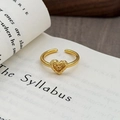 Dettaglio macro di anello a cuore dorato vintage con texture lavica su un vecchio libro - Stile Cuore Goffrato Lava (JZ6080)