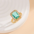 Macro view of emerald-cut green gemstone ring with pavé halo on gold setting - Gold Lake Blue Ring