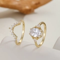 Detail van luxe vergulde kroonringen met zirkonia op minimalistische houten achtergrond - US 7 / Goud
