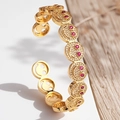 Detailansicht eines goldenen Armreifs mit Zirkonia-Smileys und roten Edelsteinakzenten - Gold Roter Rubin Zirkonia Armreif