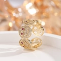 Goldener Smile-Ring mit weißen Zirkonia und roten Diamantaugen vor festlichem Bokeh-Licht - Gold Roter Rubin Zirkonia Ring