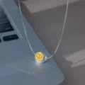 Detailansicht der gelben Emaille-Smiley-Kette auf grauem Laptop-Hintergrund - Gelb