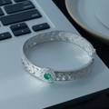 Silver open bangle with hollow lace texture and green stone centerpiece on grey background - Vintage Woven Green Gemstone Style (SL0404)