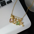 Gold pin pendant necklace with colorful heart and cross charms on a laptop surface - Gold