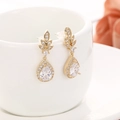 Eleganti orecchini a goccia dorati con foglie in micro-pavé su una tazza di ceramica bianca - Stile Fiore a Goccia / Oro 18K