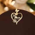 Détail macro d'un pendentif cœur doré avec motif de papillon et gravure MOM - Lettre Argent