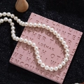 Collier élégant en perles blanches rondes sur socle rose et fond noir granuleux - Blanc (Grand)