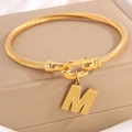 Gouden kabelarmband met hoefijzersluiting en letter M hanger op een zijden achtergrond - Gouden Armband Letter M