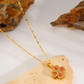 Detail view of gold clover necklace with orange gemstone and diamonds on a rock background - Red