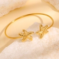 Elegante goudkleurige roestvrijstalen open armband met getextureerde zeester uiteinden - Gouden gekantelde zeester armband