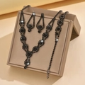 Elegant black jewelry set including layered necklace, drop earrings, and bracelet on display - Necklace Earrings And Bracelet Combination / Gunmetal