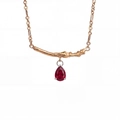 Detailed view of teardrop red zircon necklace with gold branch design on white background - July - Ruby Red