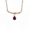 Close-up of pear-cut garnet pendant on a golden branch necklace with fine textures - January-Dark Red