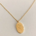 Macro detail of gold oval pendant with intricate December flower engraving on a fine chain - May Lily
