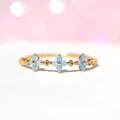 Detaillierte Nahaufnahme eines Goldrings mit zarten hellblauen Zirkonia-Blütenmotiven - Kreuz-Floraler-Stil (45)