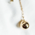 Macro del ciondolo a sfera dorata con dettaglio a cuore e perla su una catena sottile - Collana Medaglione Cuore a Sfera