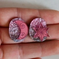 Pink glitter acrylic earrings featuring metallic moon and star patterns on finger - Pink Moon Star Style