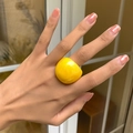 Nahaufnahme eines breiten neongelben Acrylrings am Finger eines Models bei warmem Licht - Gelb
