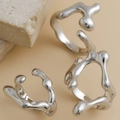 Nahaufnahme unregelmäßiger silberner Ringe im Liquid-Lava-Stil auf strukturiertem Stein - Flüssig Minimalistisch Set / Silber