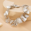 Macro detail of textured silver petal necklace on a minimalist geometric display stand - Silver
