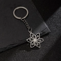 Silver stainless steel daisy flower keychain with hollow carved petals on stone surface - Steel