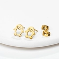 Macro detail of cute golden stainless steel penguin stud earrings on white ceramic tray - Gold