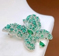 Detail van vlinderbroche met groene stenen, zirkonia en een druppelvormige hanger - Smaragd