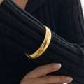 Close-up of polished gold wide cuff bracelet worn over a stylish black textured sleeve - Thick Polished Style (2441) / Gold