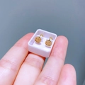 Nahaufnahme kleiner goldener Smiley-Ohrstecker in weißer Box mit Hand als Referenz - Smiley