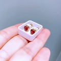 Makroaufnahme kleiner goldener Herzohrringe mit roten Edelsteinen in einer Displaybox - Rotes Zirkonherz
