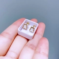 Nahaufnahme kleiner goldener Bärenohrstecker in einer Box, gehalten von Fingern - Teddybär